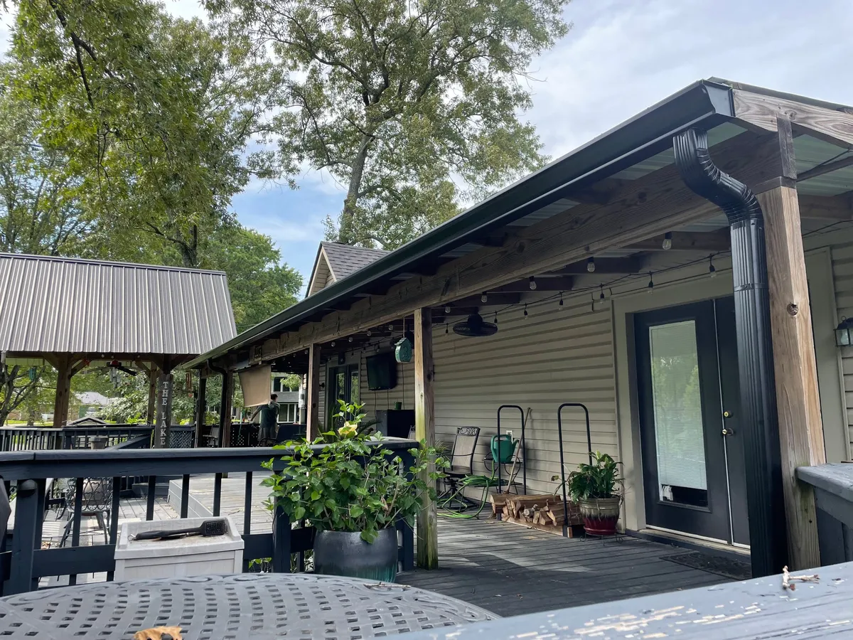 Covered deck with a black gutter and downspout and string lights overhead
