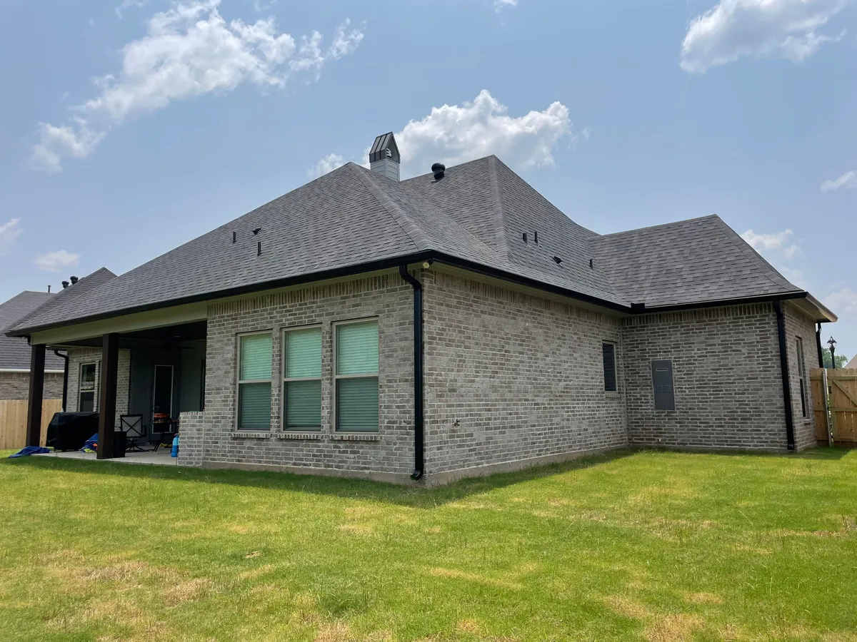 Rear elevation of a brick home with a covered patio and dark gutters