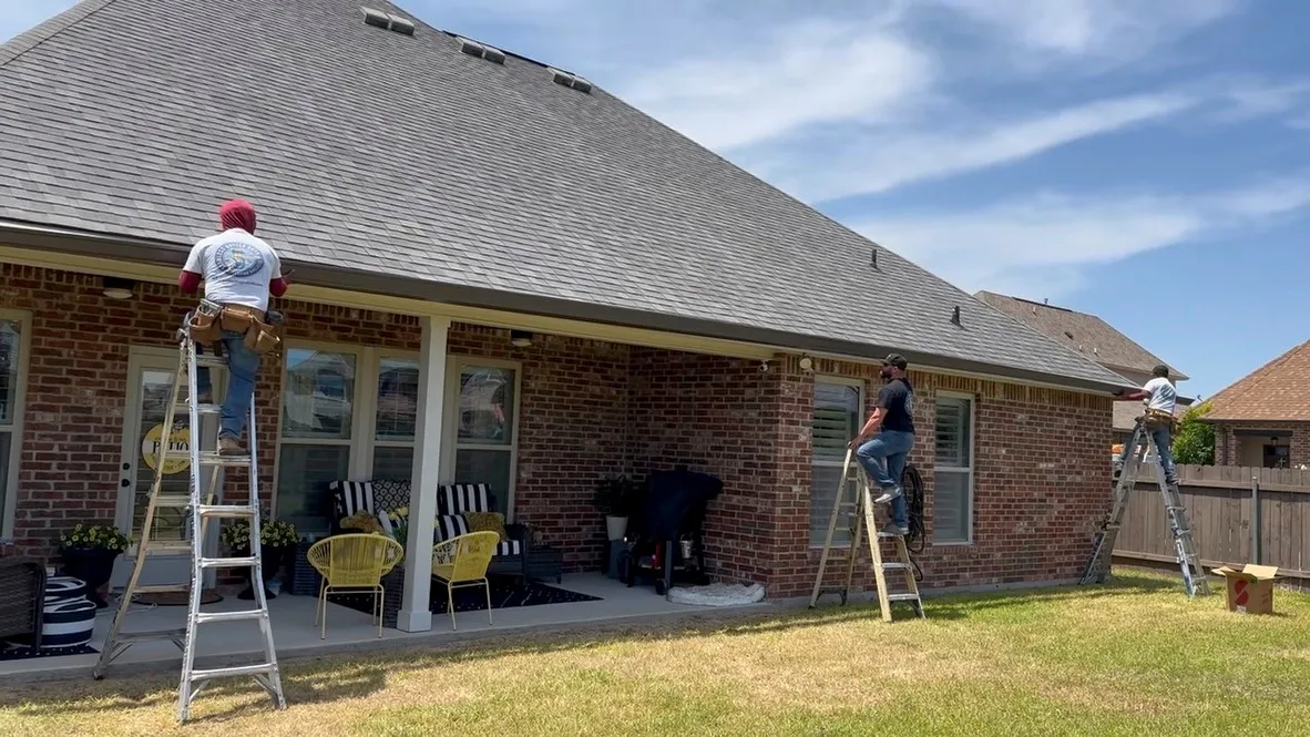 Three Seamless Gutter Guys installers working together along the gutter line of a brick home’s covered patio.