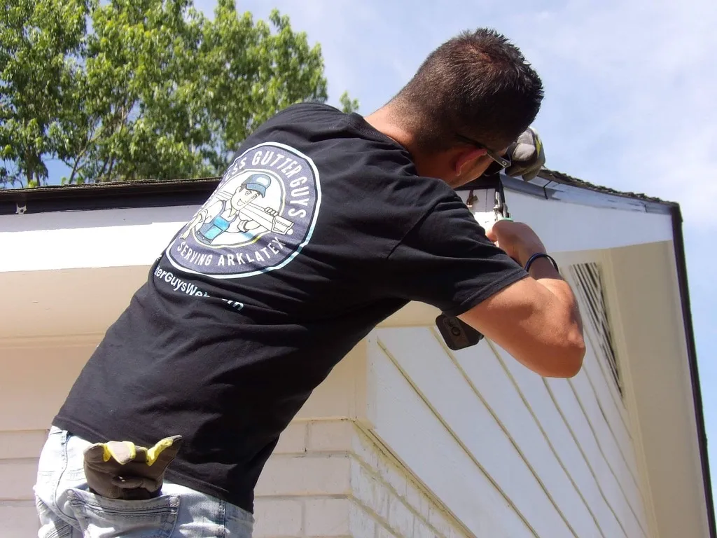 A Seamless Gutter Guys crew member in a branded shirt working at a gutter corner on a home.