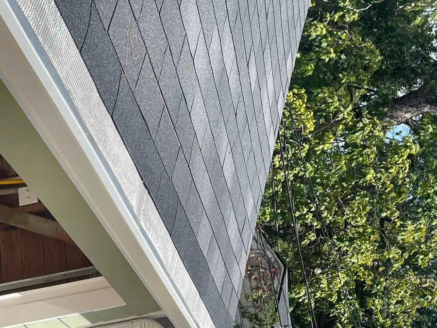 Close-up along an installed gutter, where a fine stainless micro-mesh guard panel is set between the gutter lip and the shingle edge