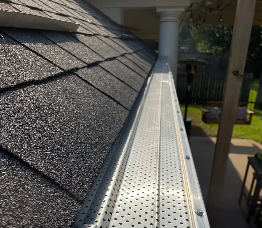 Close-up along an installed gutter, where a perforated aluminum guard panel sits over the gutter against the shingle edge