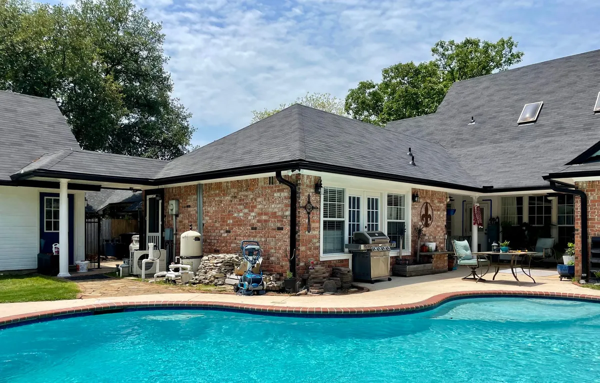 Brick home with a swimming pool and black gutters along the rear elevation