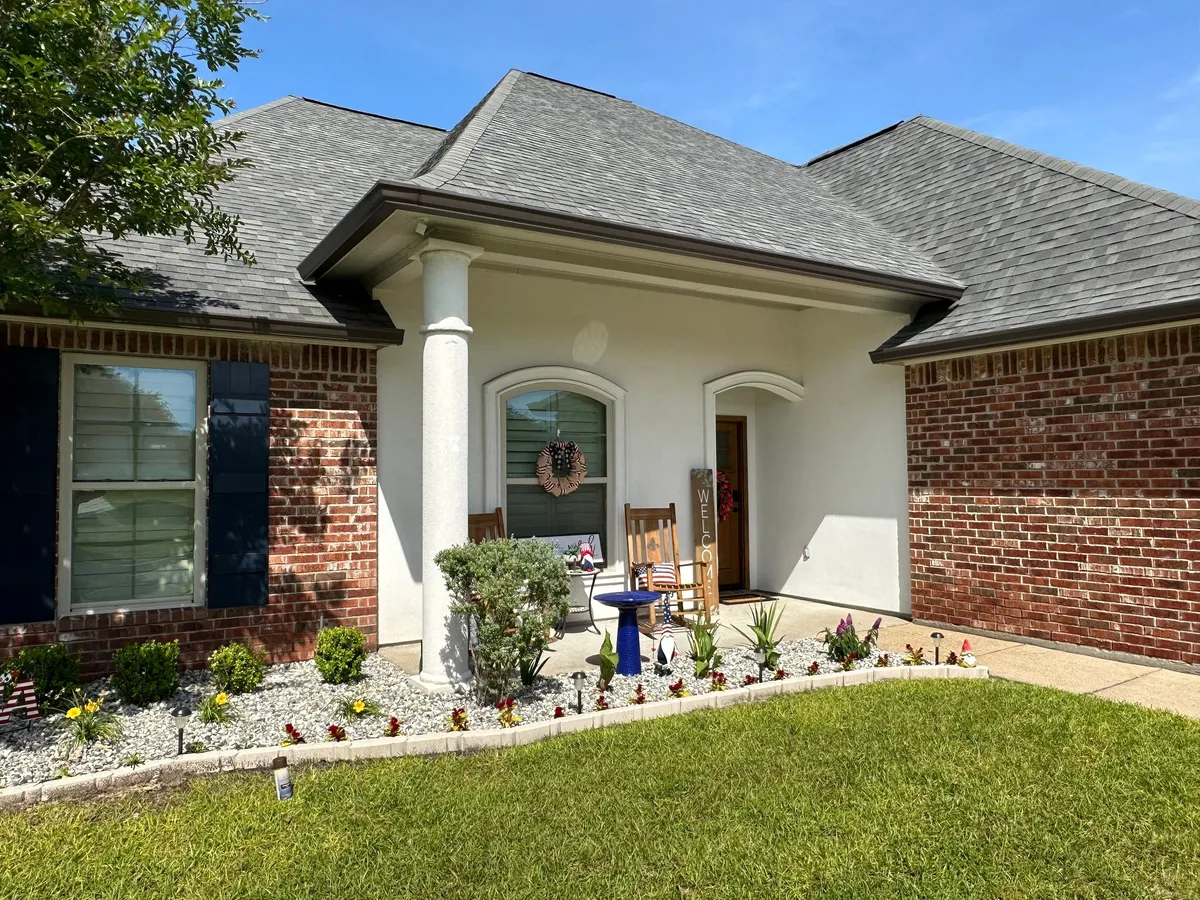 After: The same home from a closer angle, with a dark bronze seamless gutter running along the porch roofline and the eave