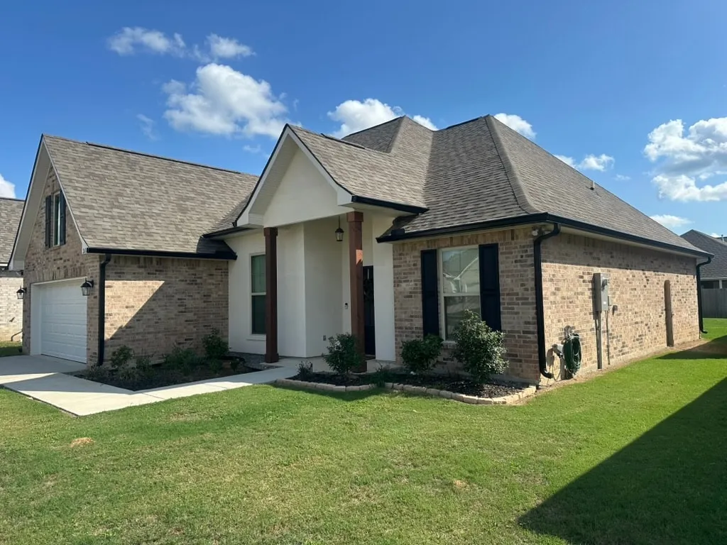 After: The same Shreveport brick and stucco home with black seamless gutters along the roofline and black downspouts at the corners